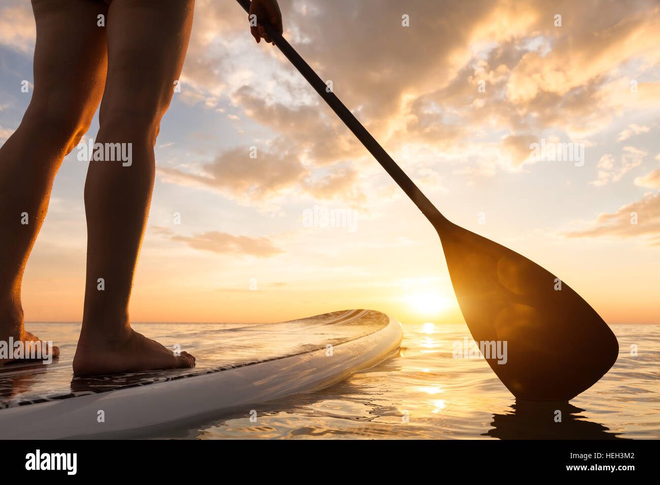 Paddle boarding auf einem ruhigen See mit warmen Sommerfarben Sonnenuntergang, Nahaufnahme Beine aufstehen Stockfoto