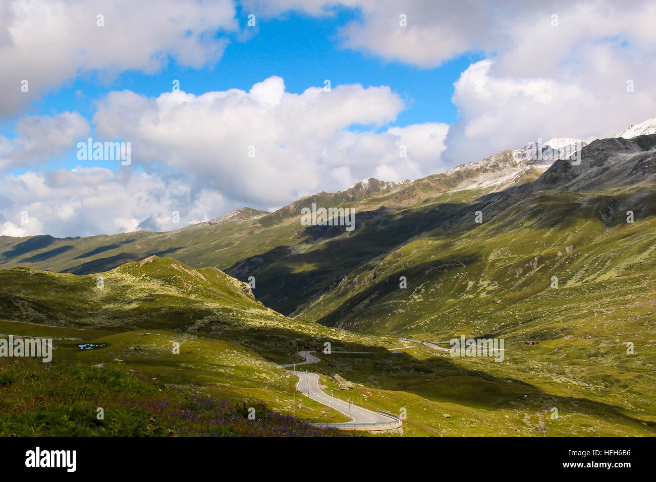 Sehen Sie sich auf ein Schweizer Alpenlandschaft mit einer kurvenreichen Straße und bewölktem Himmel Stockfoto