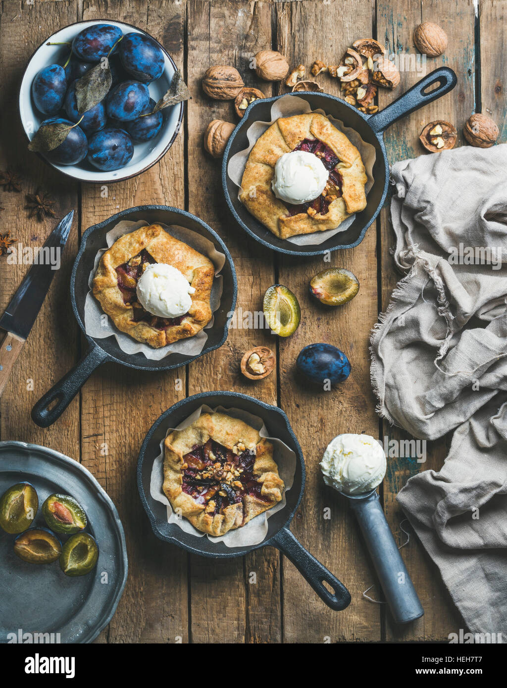 Pflaume und Walnuss Crostata pie mit Eisportionierer in einzelnen Gusseisen Pfannen über rustikalen Holztisch, Ansicht von oben. Slow-Food-Konzept Stockfoto