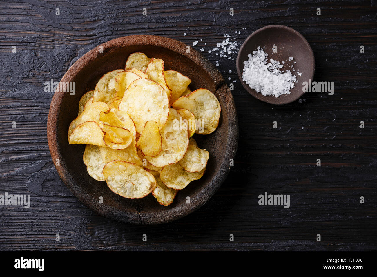 Hausgemachte knusprige Kartoffelchips und Meersalz auf dunklem Holzhintergrund Stockfoto