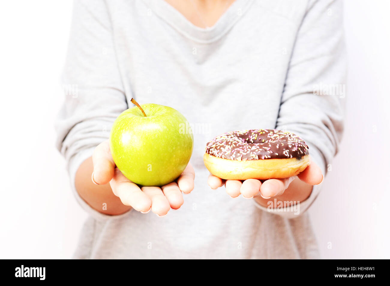 Gesunden Lebensstil oder Ernährung Konzept mit jungen Frau, die in den Händen halten, einen grünen Apfel und einen donut Stockfoto
