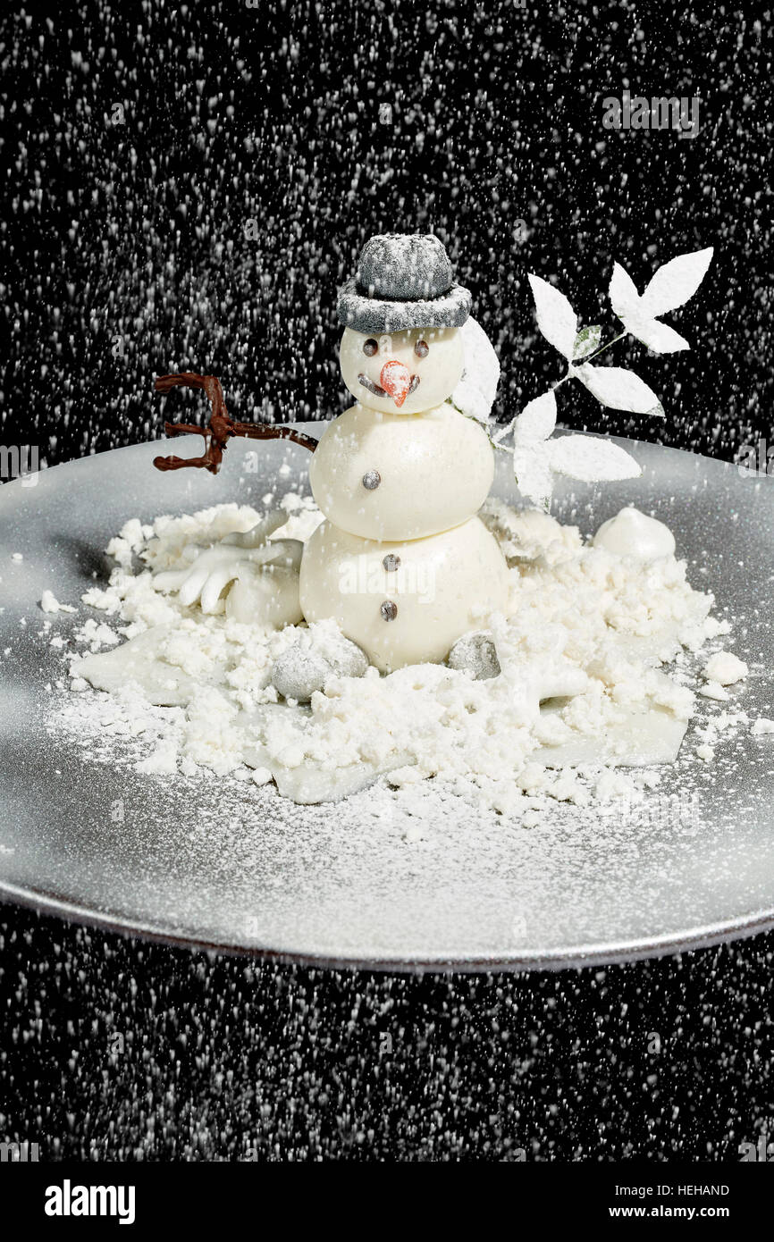 Weiße Schokolade Schneemann Weihnachten Dessert Puderzucker Schneefall Winter kalt schwarz Hintergrund Zweig Hutplatte Stockfoto