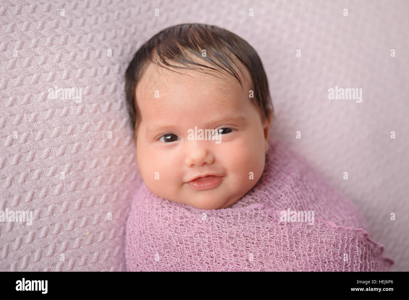 Porträt von sechs Wochen alten, lächelndes Babymädchen. Sie ist beschützend in einem Lavendel farbige wickeln und auf einem rosa Decke liegen. Stockfoto