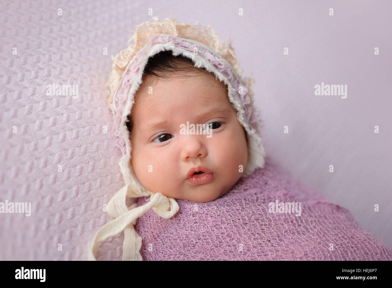 Porträt eines Mädchens alert, sechs Wochen altes Baby. Sie ist in einem Lavendel gepuckt Wrap und trägt eine Spitze Mütze. Stockfoto