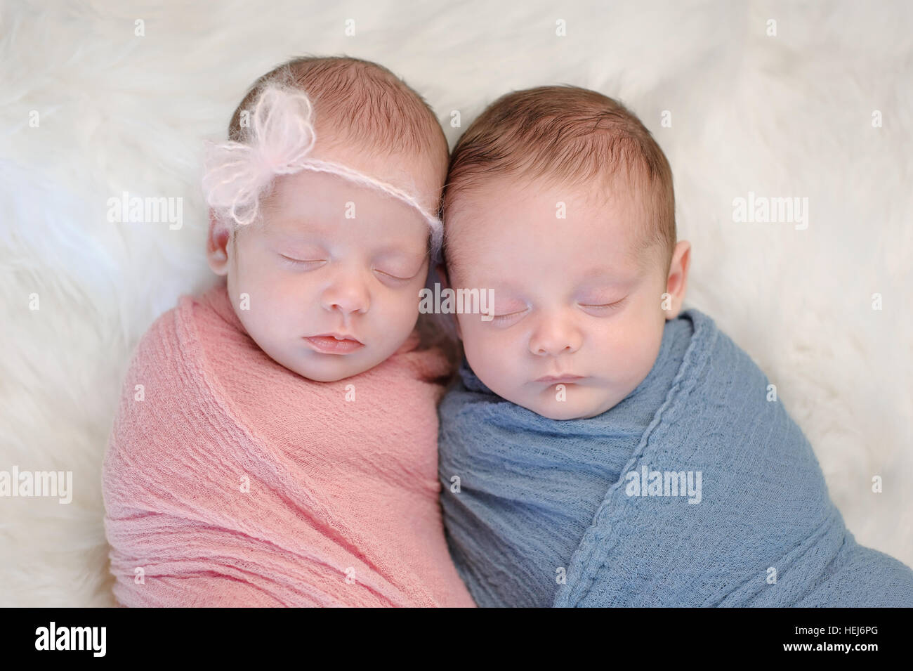 Zwei Monate alt, brüderlichen Twin, Bruder und Schwester Babys gepuckt in rosa und blau Wraps und schlafen auf einem Schaffell-Teppich. Stockfoto