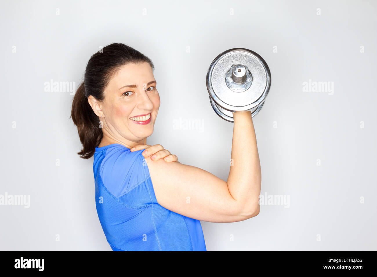 Fröhlich und stolz auf gewöhnliche Frau in hell blau Sportoutfit Heavy-Metal-Gewicht heben, halten ihre New Years resolution Stockfoto