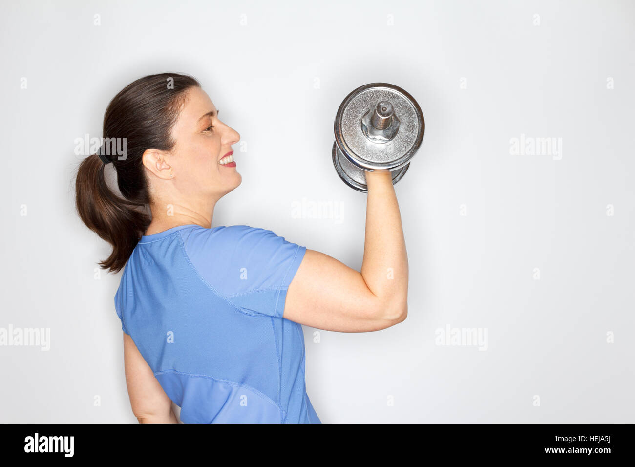 Stolz lächelnd Erwachsene Frau im Sportoutfit Ausübung durch eine schwere Hantel, hellem Hintergrund, viele textfreiraum anheben Stockfoto