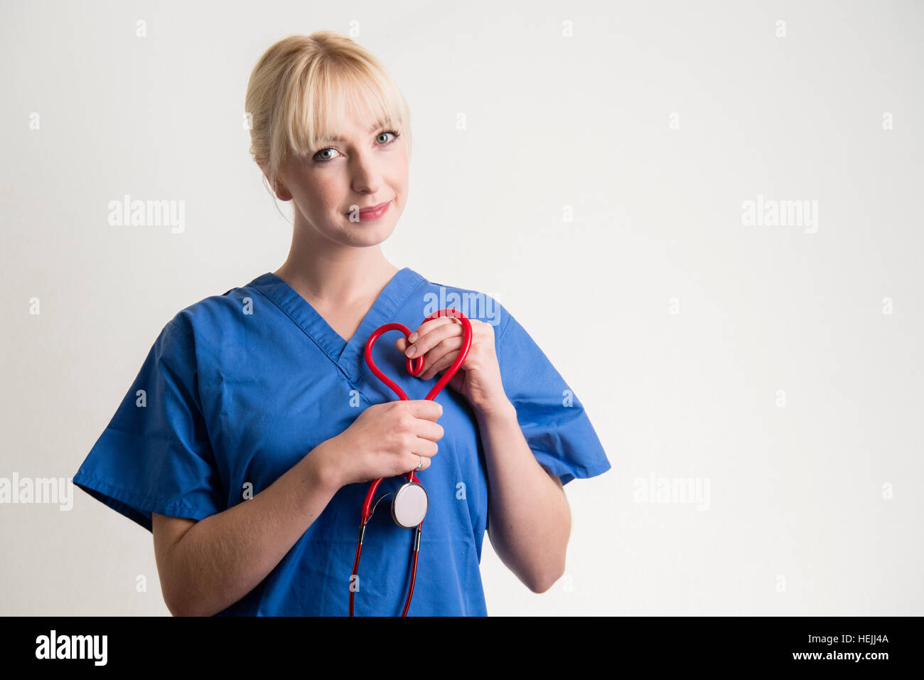 UK Health Care Professionals: A National Health Service (NHS) Frau Krankenschwester hält eine rote Stethescope in der Form eines Herzens. Stockfoto