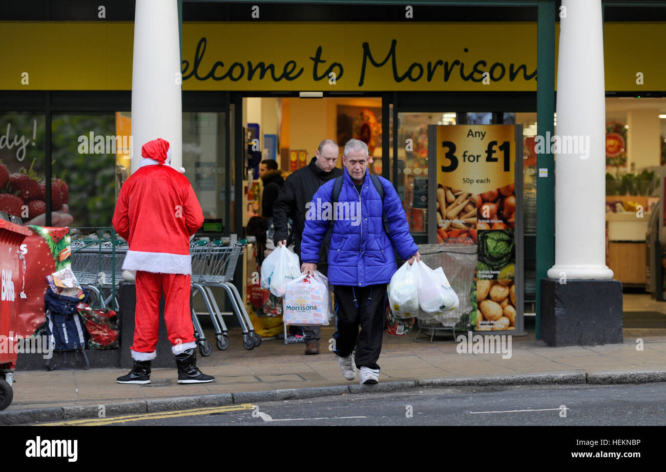 Brighton UK 23. Dezember 2016 - beladen mit Taschen Shopper pass von einem Big Issue Verkäufer als Weihnachtsmann verkleidet, beim Verlassen eines Safeway-Supermarkts in Brighton mit heute voraussichtlich die verkehrsreichsten Weihnachts-Essen shopping-Tag der festlichen Zeit in Großbritannien Credit: Simon Dack/Alamy Live News Stockfoto