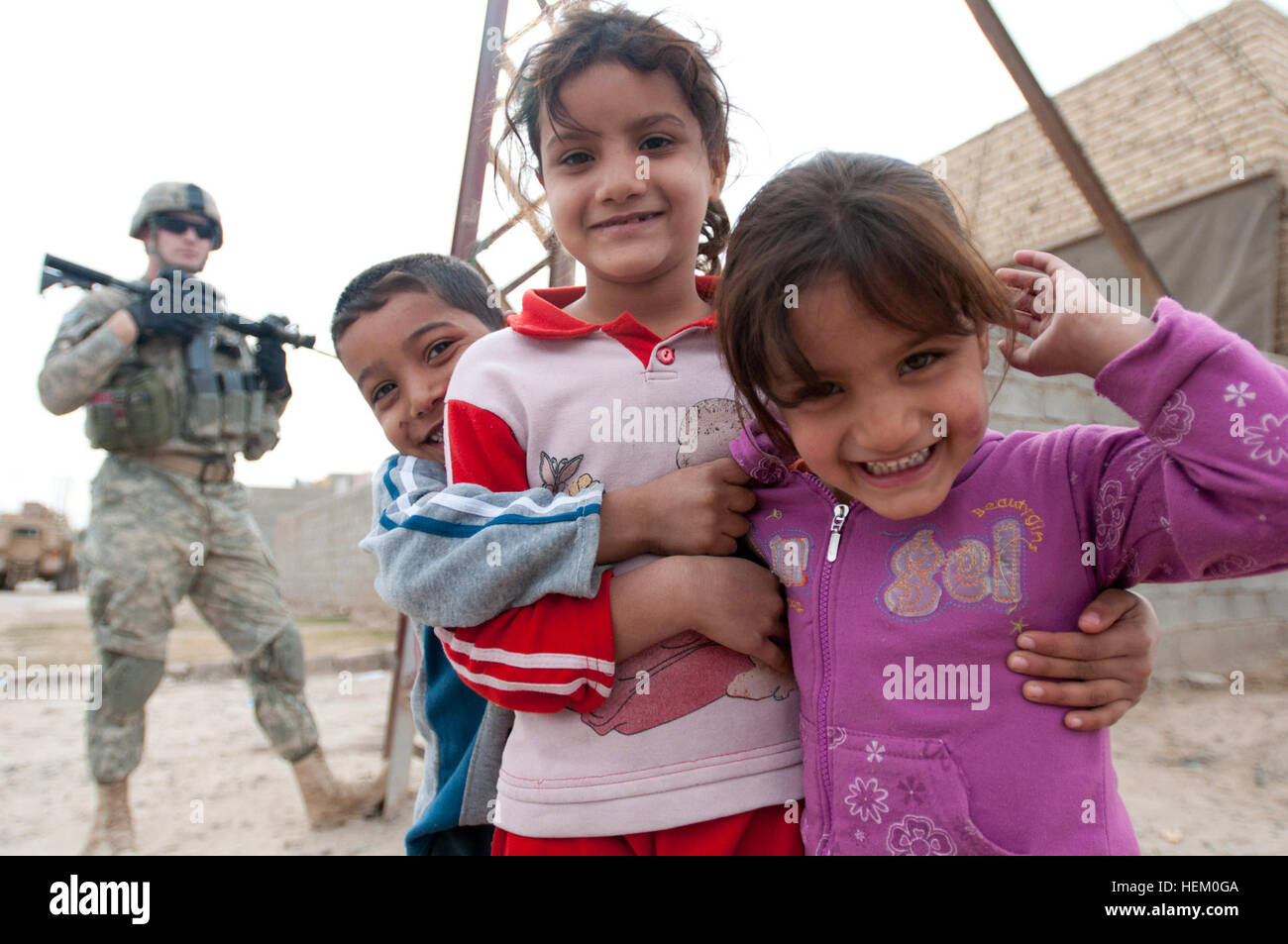 Drei irakische Kinder umarmen sich und kichern wie ein Fallschirmjäger Sicherheit im Hintergrund in einem Dorf nördlich von Bagdad am 17. November zieht. Mit der US Army Mission aus den letzten acht Jahren im Irak ist der Anblick von amerikanischen Soldaten für irakische Jugendliche an der Tagesordnung. Infanteristen, C Company, 2. Bataillon, 325. Airborne Infanterie-Regiment, 2. Brigade, 82. US-Luftlandedivision, reiste in das Dorf von Camp Taji, sich zu informieren über die jüngsten Anschläge im Bereich zugewiesen. Die 2. Brigade ist die letzte Brigade in Bagdad und weiterhin mit den irakischen Sicherheitskräften, Geschäftsreisehotel partner Stockfoto