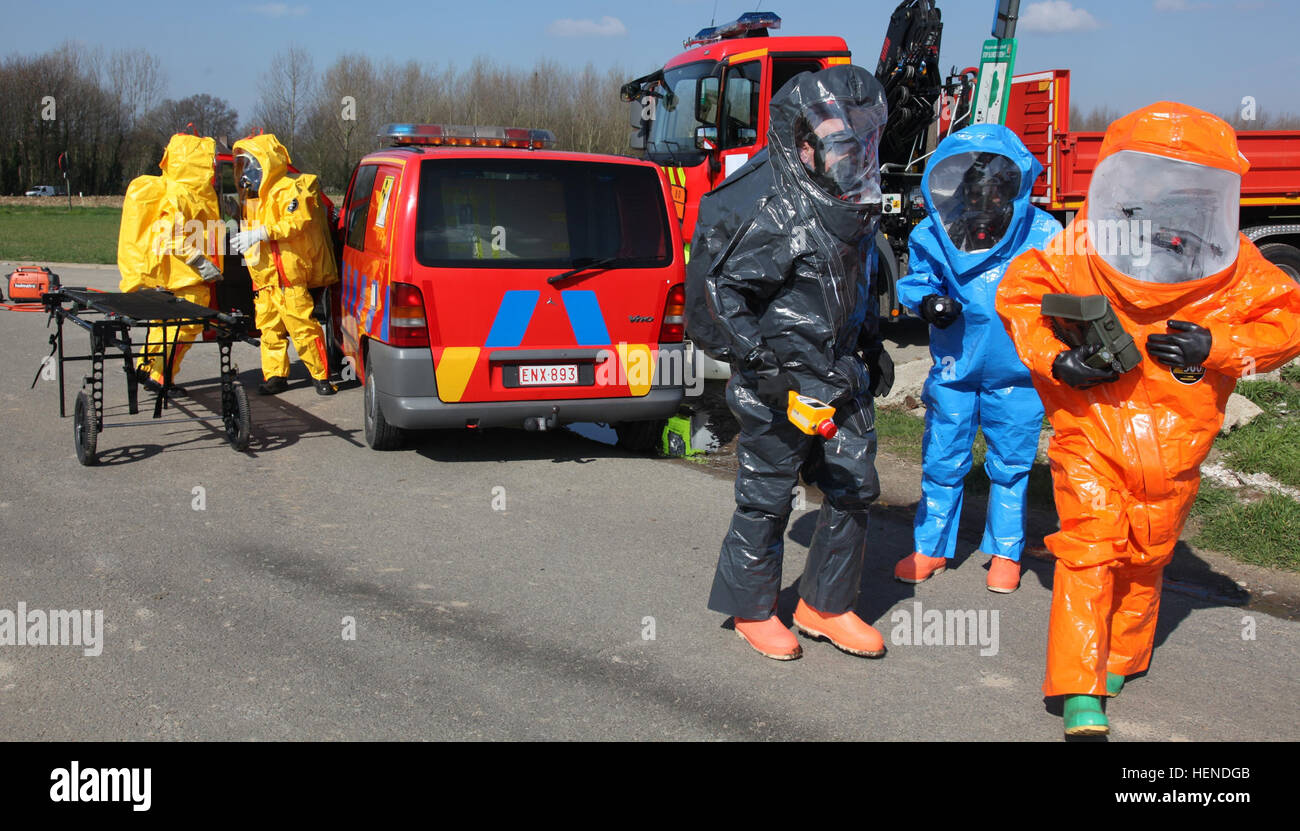 Im Vordergrund, den 773rd Civil Support Team Soldaten aus dem 7. zivile Unterstützung Befehl beenden anfängliche Überwachung und Beurteilung von einem simulierten radiologische und chemische Spill, verursacht durch eine Multiple-Fahrzeug-Unfall beim chemischen biologische radiologische Nuclear Training mit Zaventem Feuerwehr während der fünften, bereiten jährliche "CBRN-Woche" training Übung 24-28 März 2014, während im Hintergrund, Zaventem FD Feuerwehr simuliertes Opfer aus einem der Fahrzeuge zu evakuieren. In "Level A" HAZMAT-Anzüge in schwarz, Army Staff Sgt John Gribble, Umfrage Team Unteroffizier, 773r Stockfoto