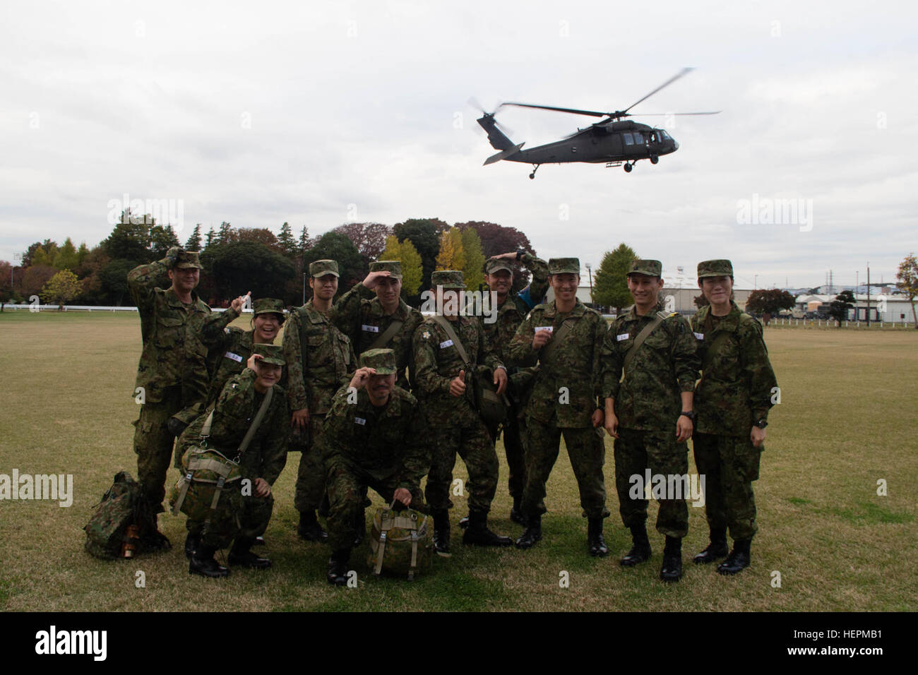 Japan-Ground Self-Defense Force (JGSDF) Reserve Komponente Kandidaten aus dem 117. Training Bataillon, JGSDF, festhalten, ihre Kopfbedeckung als UH-60 Black Hawk-Hubschrauber von US-Armee Japans (USARJ) Aviation Battalion steigt für eine Landung bei Sagami General Depot, Japan, 19. November 2015. Früher an diesem Tag flog die Kandidaten von der 117. Training Bataillon in Camp Takeyama, Japan, nahmen an einer Reihe von Veranstaltungen, die ihren in einem bilateralen Eingriff durchgeführt durch die Army Reserve Engagement Team-Japan (ARET-J Höhepunkt). ARET-J verpackt mit Präsentationen, am Fuß Stockfoto