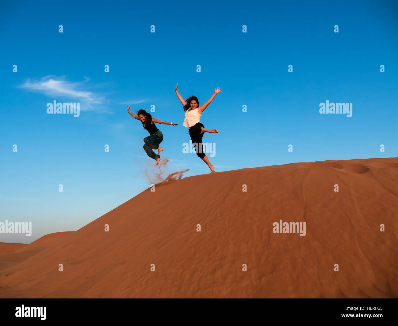 Zwei junge Frauen, die einen Sprung von Sanddüne in der Wüste, Sharqiya Sande oder Wahiba Sands, Al Raka, Oman Stockfoto