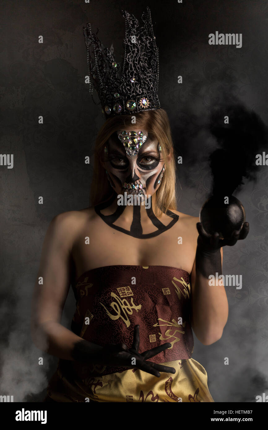 Tag der Toten kreative Make-up in Candy-Schädel-Stil mit gotischen Krone, hält Rauchen schwarze Kristallkugel Stockfoto
