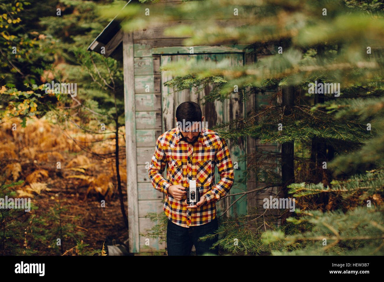 Junger Mann stand in der Nähe der Hütte im Wald, Fotografieren mit der Kamera in der Nähe von Shaver Lake, Kalifornien, USA Stockfoto