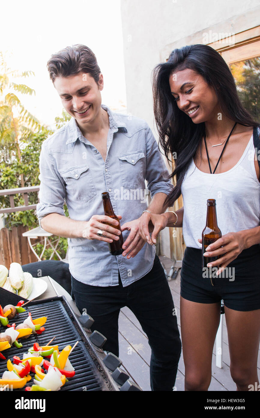 Junges Paar im Freien, mit Bierflaschen, Kochen am Grill Stockfoto