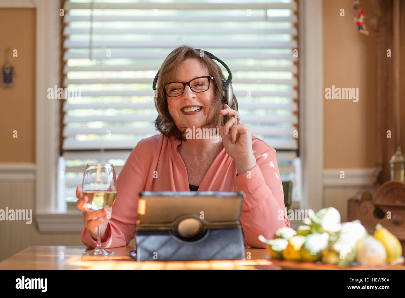 Ältere Frau am Küchentisch Kopfhörer anhören Stockfoto