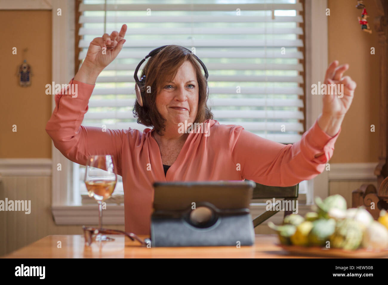 Ältere Frau am Küchentisch hören und tanzen zu Kopfhörer Stockfoto