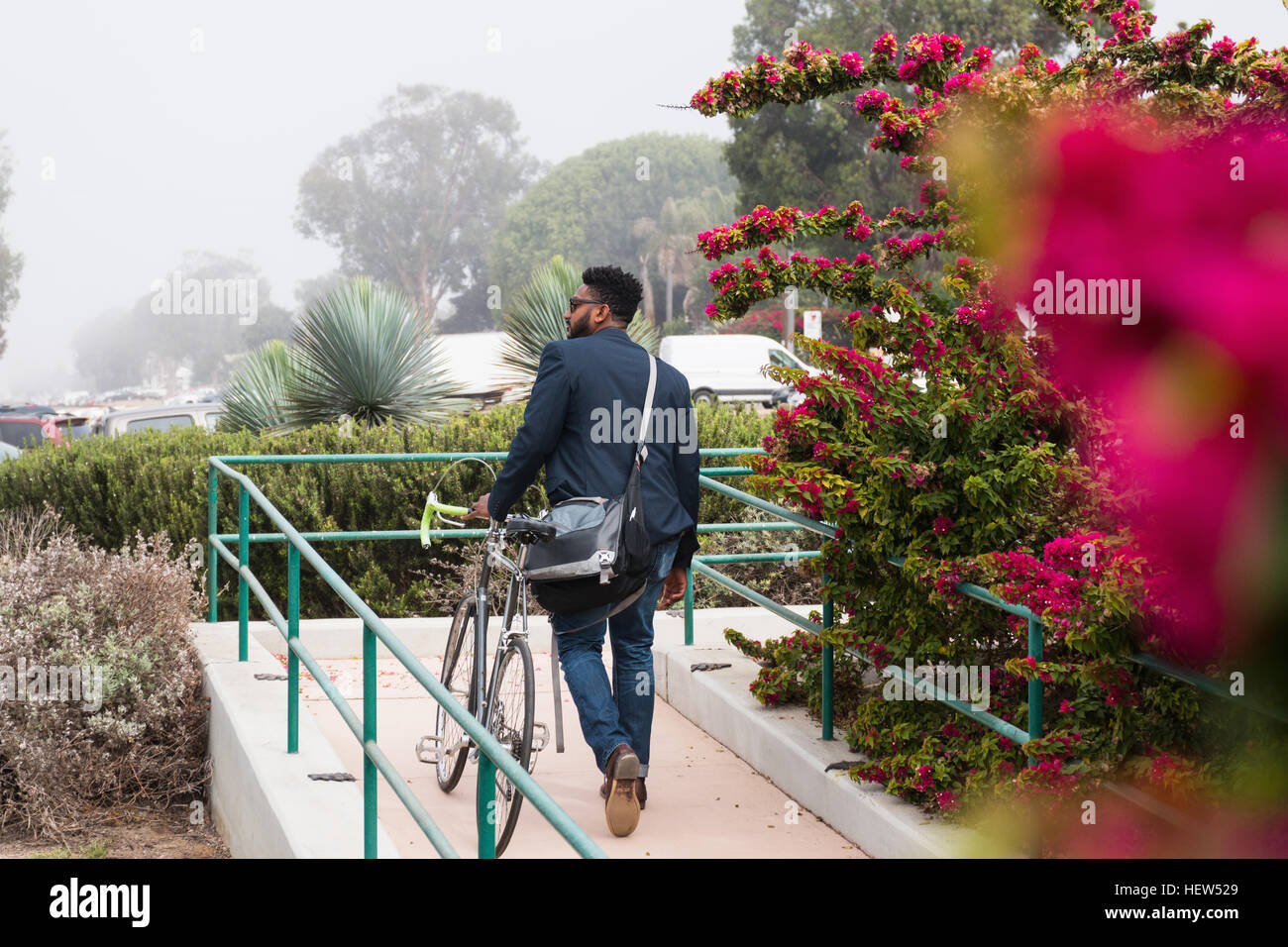 Junger Mann zu Fuß im Freien, mit dem Fahrrad, Rückansicht Stockfoto
