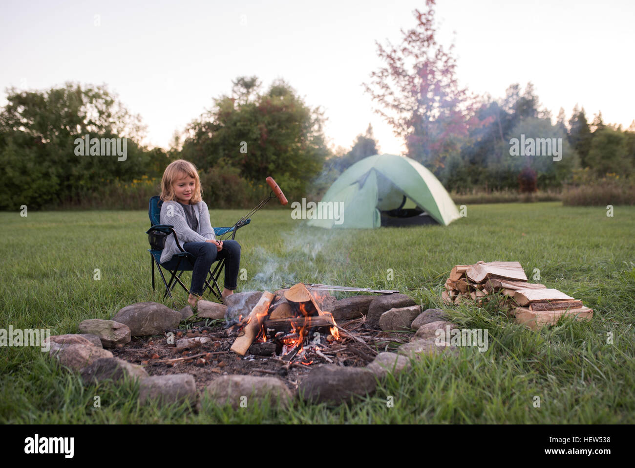 Junges Mädchen saß am Lagerfeuer, Würstchen Kochen Stockfoto