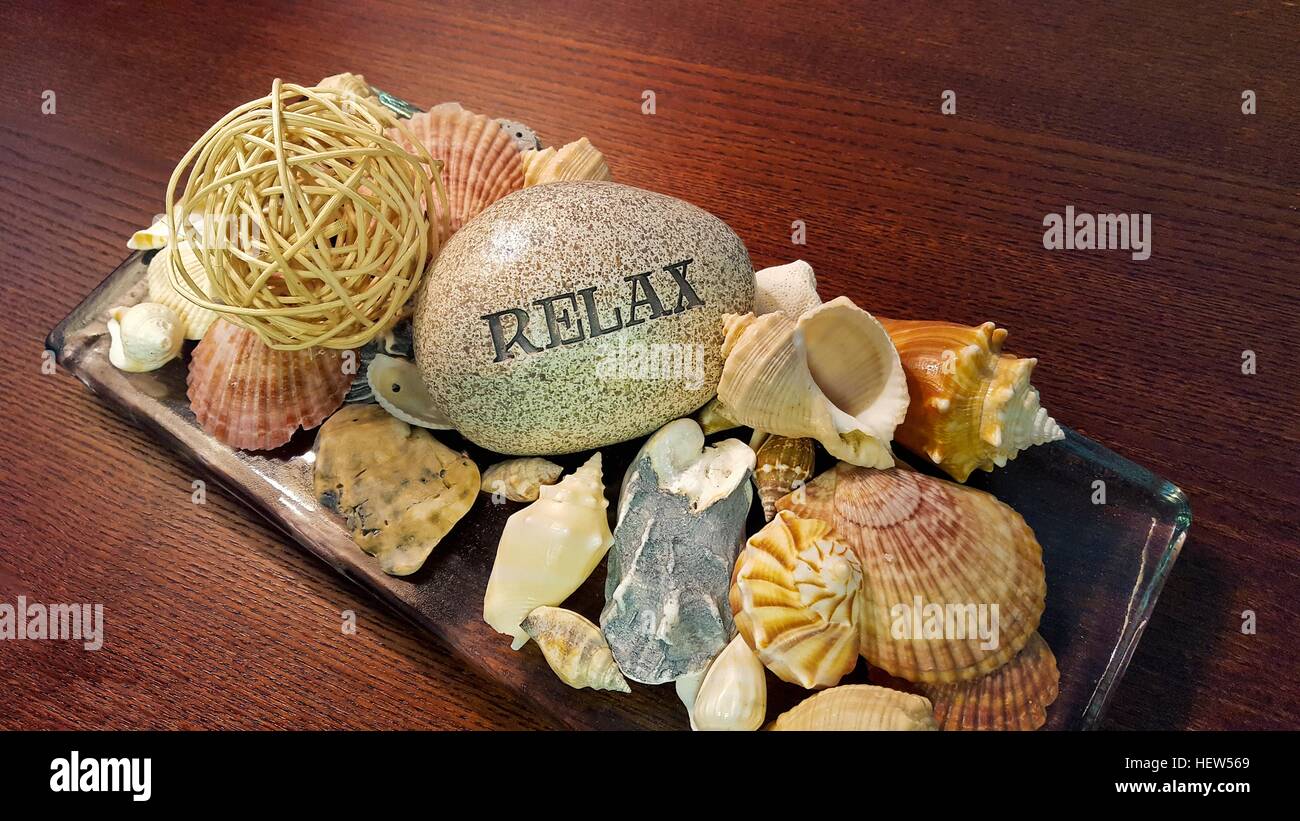 Spa-Stein mit Wort entspannen geschnitzten drauf mit Muscheln auf Holzplatte Stockfoto