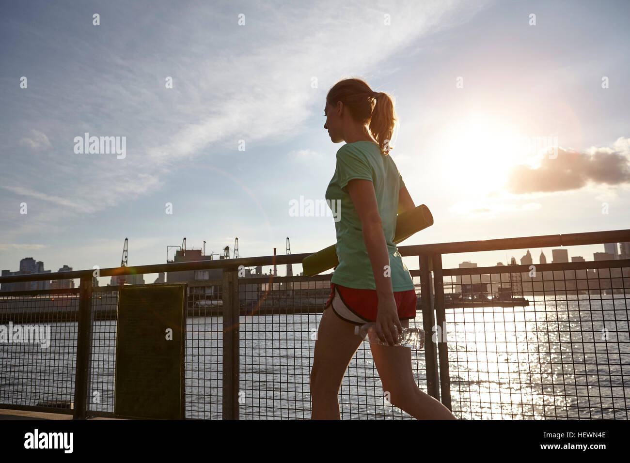 Frau zu Fuß auf Pier mit Yoga-Matte, Manhattan, New York, USA Stockfoto