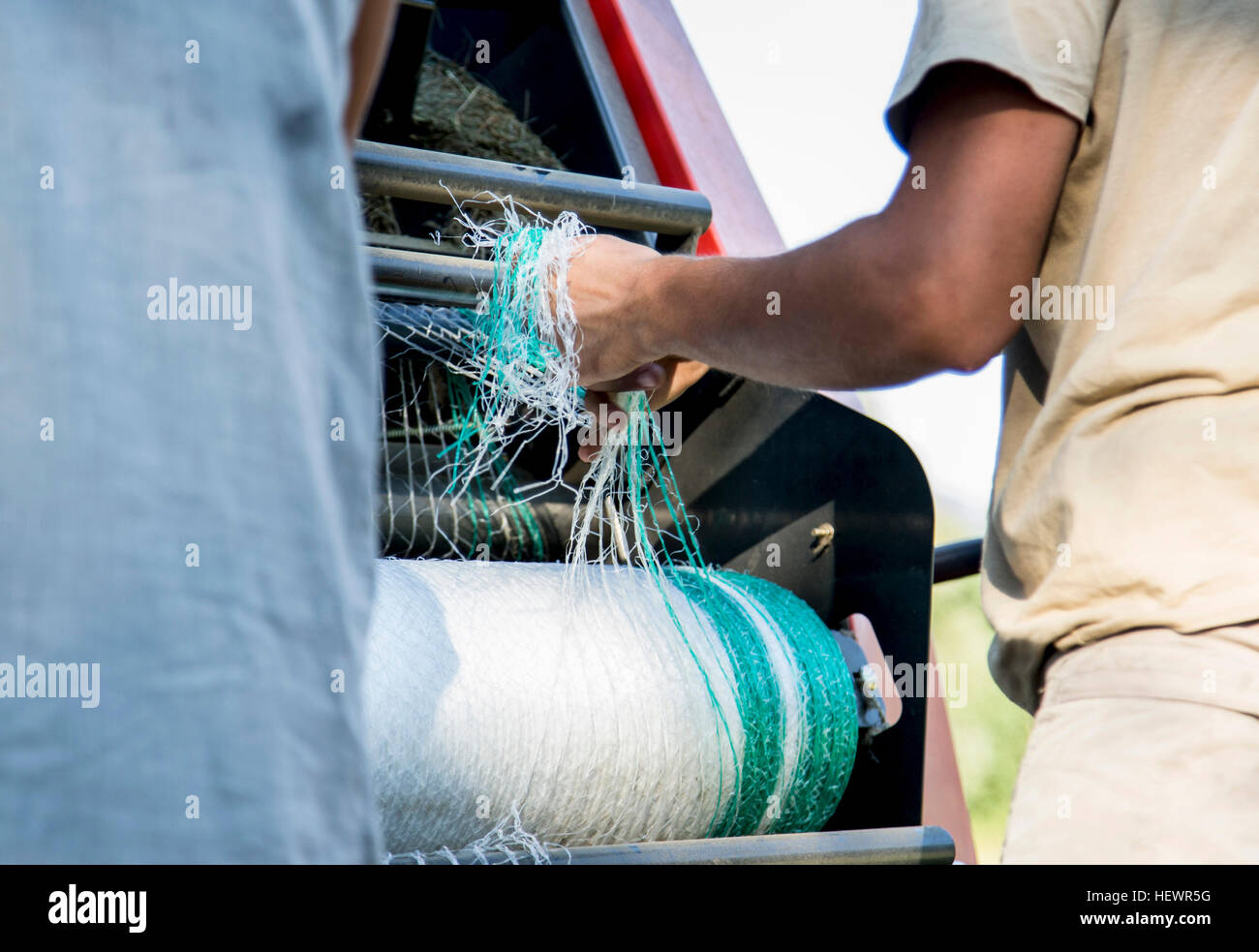 Aufnahme von zwei männlichen Landarbeitern entwirren Netting im Heu Ballenpresse beschnitten Stockfoto