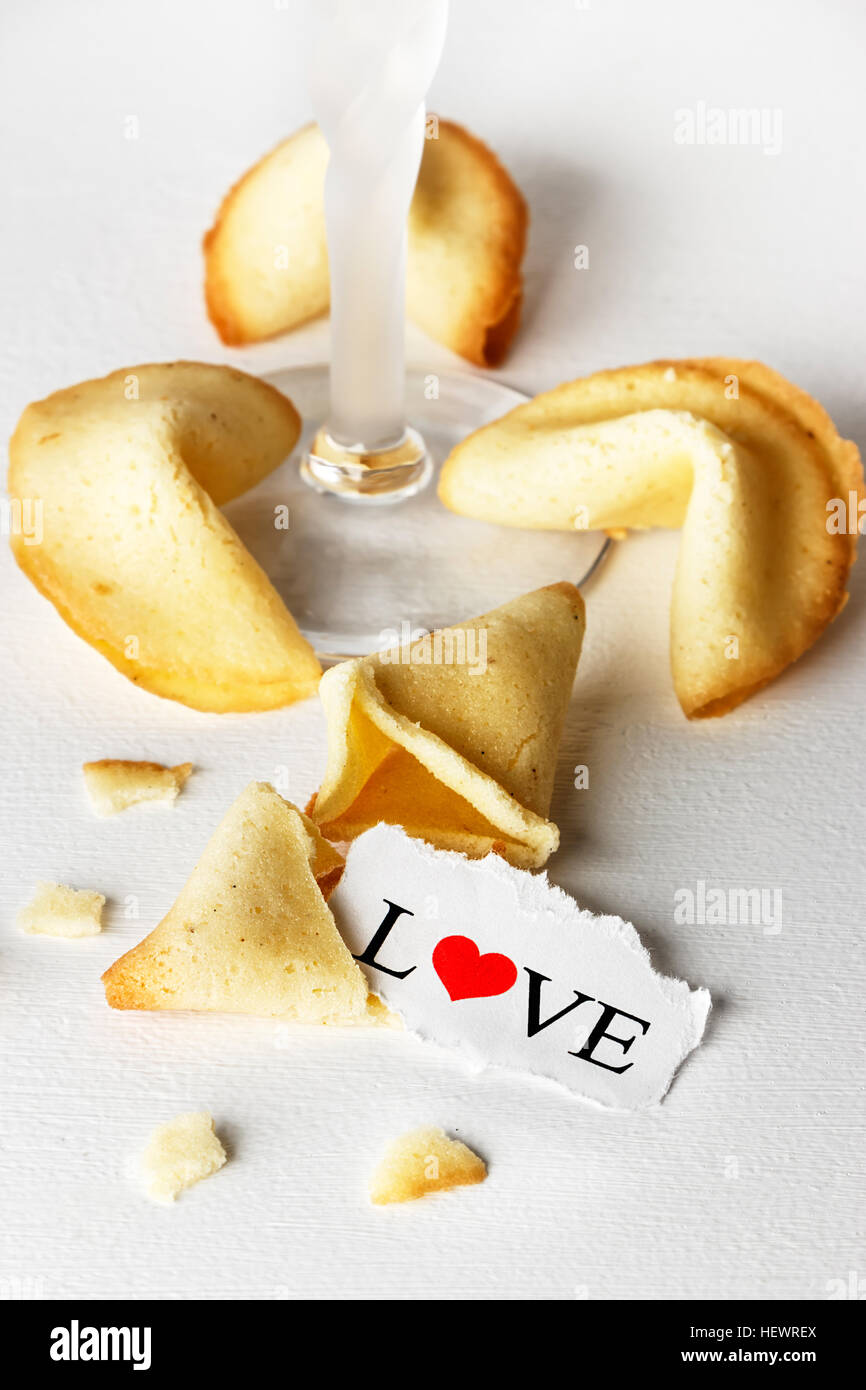 Cookies mit dem Wort Liebe geschrieben auf ein Blatt Papier und einem Glas Champagner wie Tortellini geformt. Vertikales Bild. Stockfoto