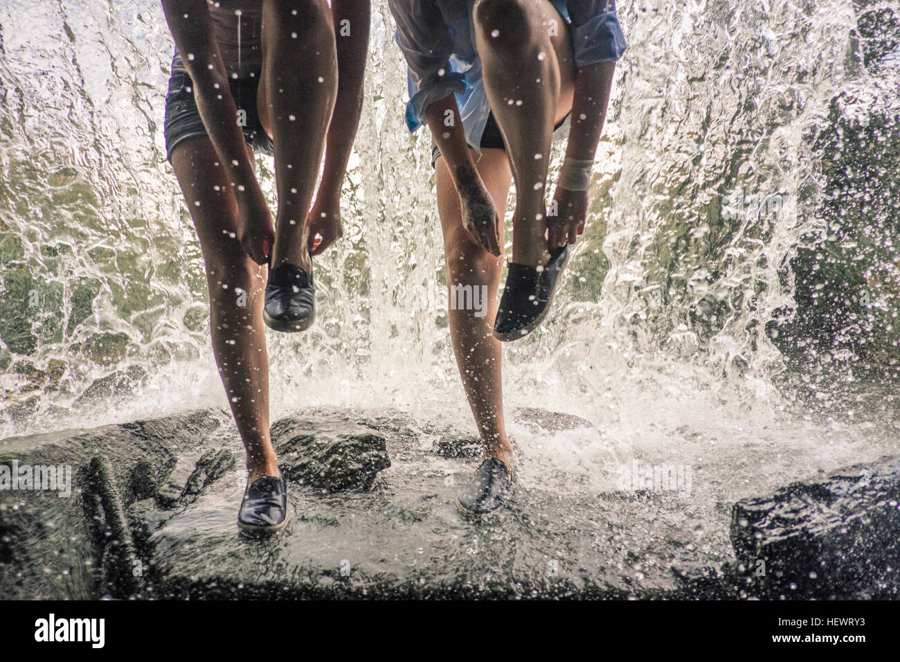 Taille abwärts von Mädchen auf Felsen Wasserfall Schuhe anziehen Stockfoto