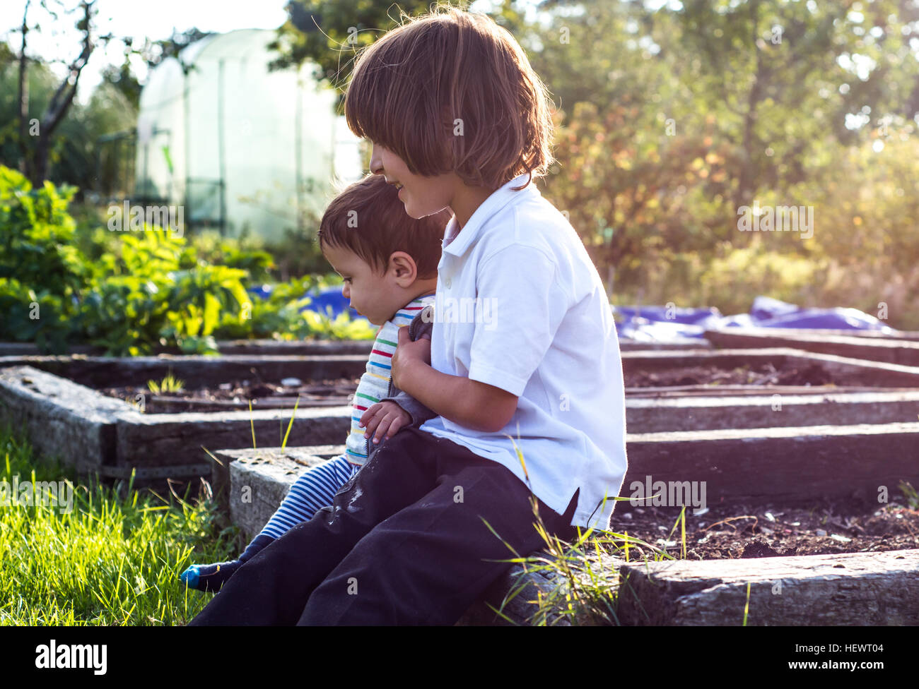 Junge und seinem kleinen Bruder Zusammensitzen im sonnigen ländlichen Garten Stockfoto