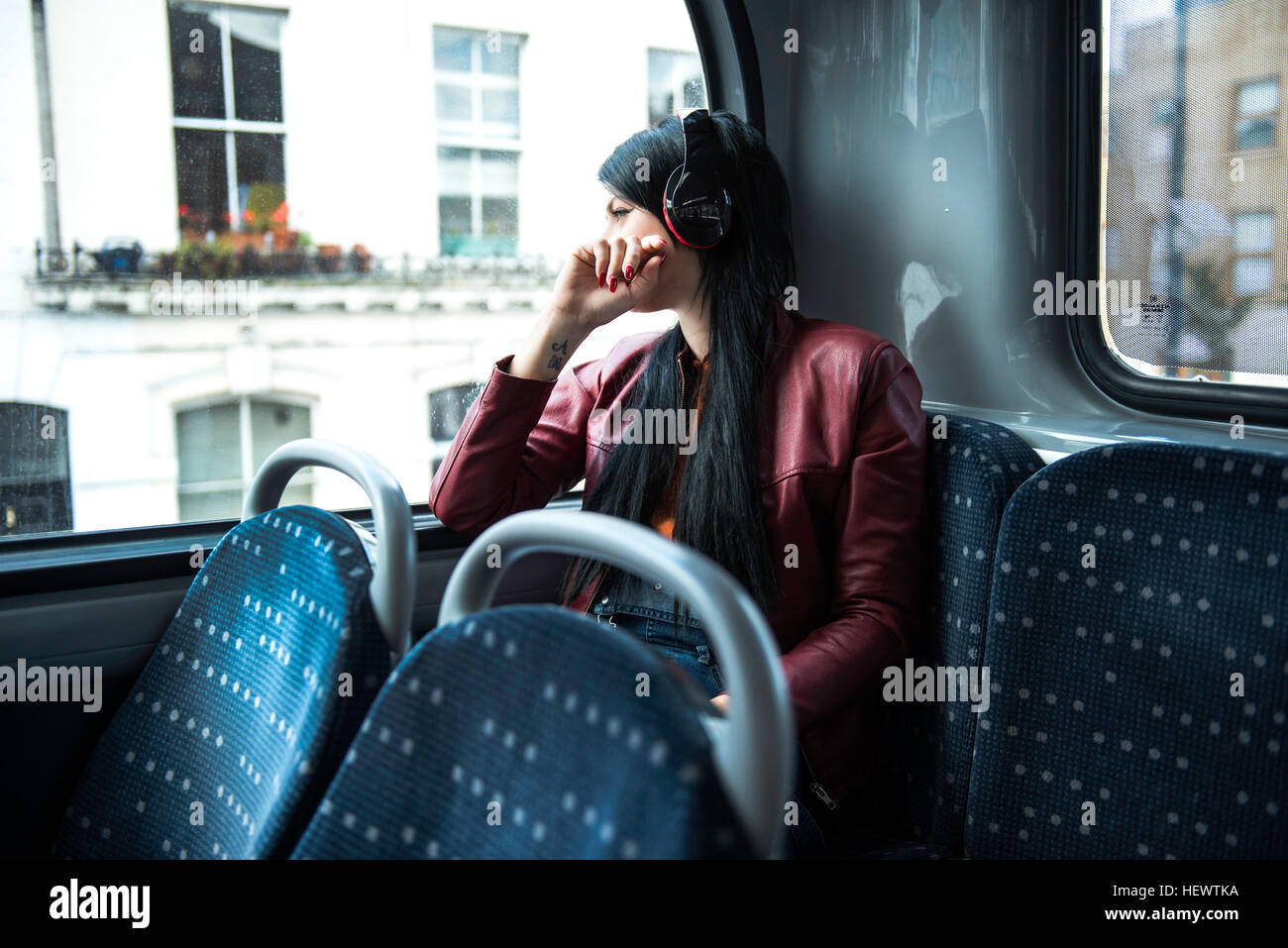 Junge Frau sitzt im Bus, tragen von Kopfhörern, Blick aus Fenster Stockfoto
