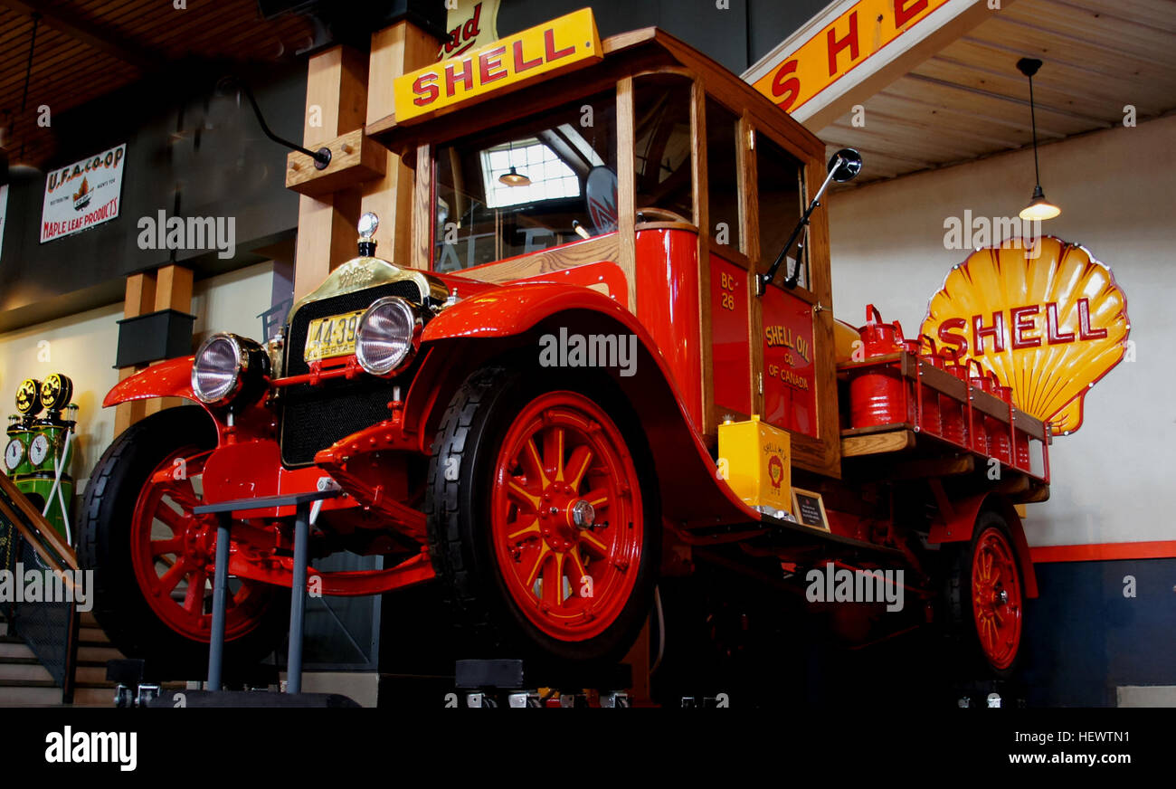Ein Foto von Shell Tanker aus dem Jahr 1926, auf dem amerikanische Luxusautos auf einer Autoausstellung im Benzoline Alley Heritage Park, Calgary, gezeigt werden. Das Bild zeigt klassische Fahrzeuge und zeitspezifische Details wie einen weißen Lkw und alte Gaspumpen. Stockfoto