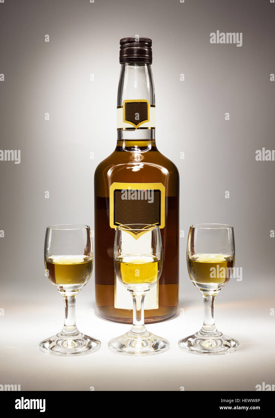 Drei kleine Gläser vor eine Flasche voller Alkohol trinken. Stockfoto
