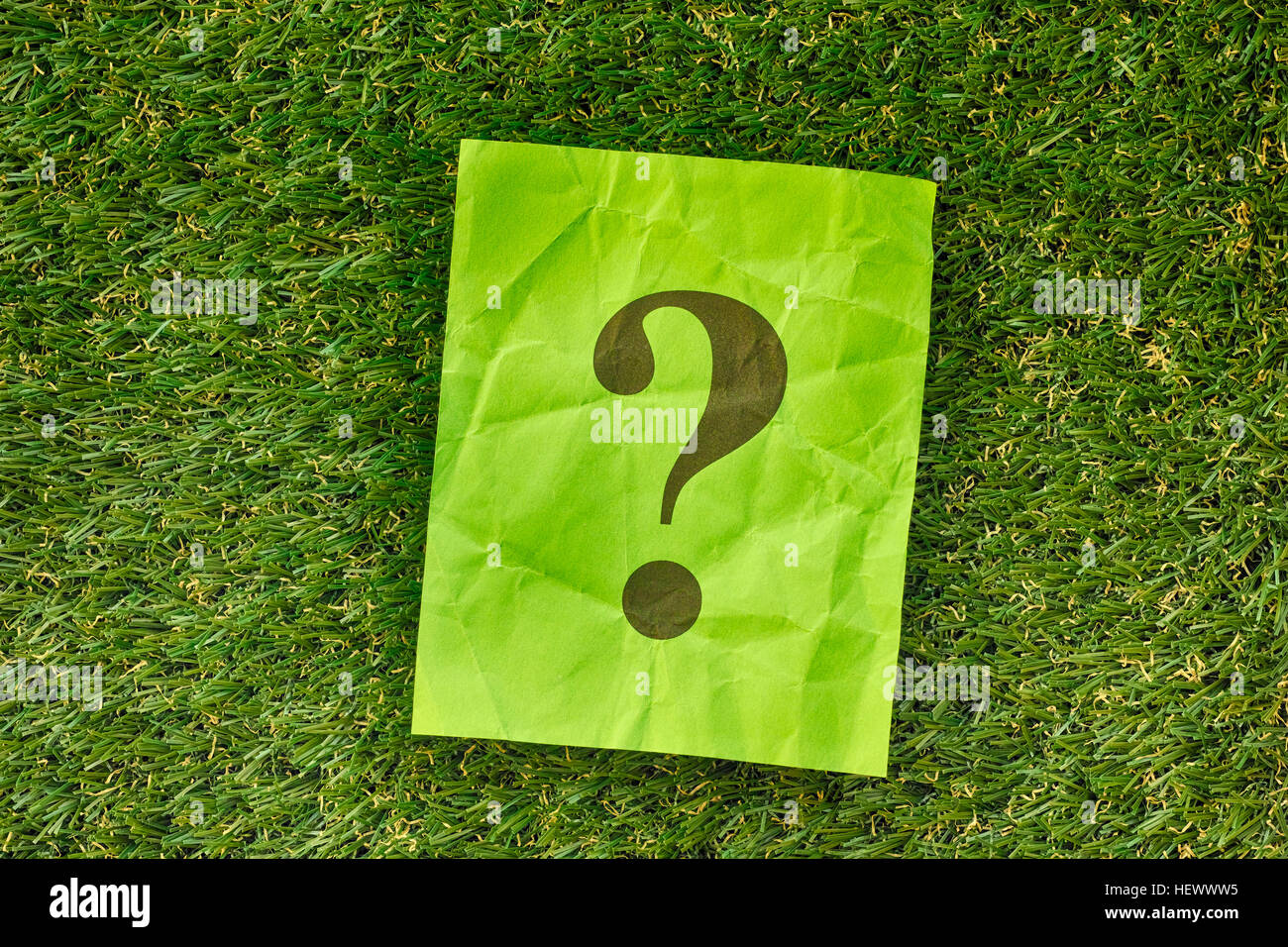 Grünes Papier-Schuldbrief mit Fragezeichen auf dem grünen Rasen. Hautnah. Stockfoto