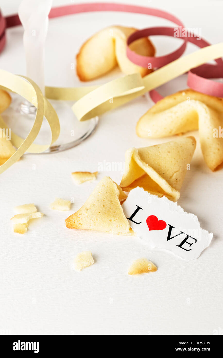 Cookies mit dem Wort Liebe auf ein Blatt Papier und ein Glas Champagner mit Streamer geschrieben wie Tortellini geformt. Vertikales Bild. Stockfoto