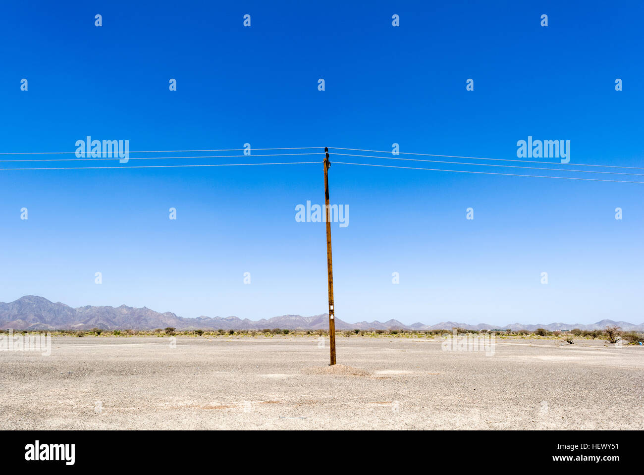 Ein einsamer Strom Pole läuft durch eine flache und karge Wüste. Stockfoto