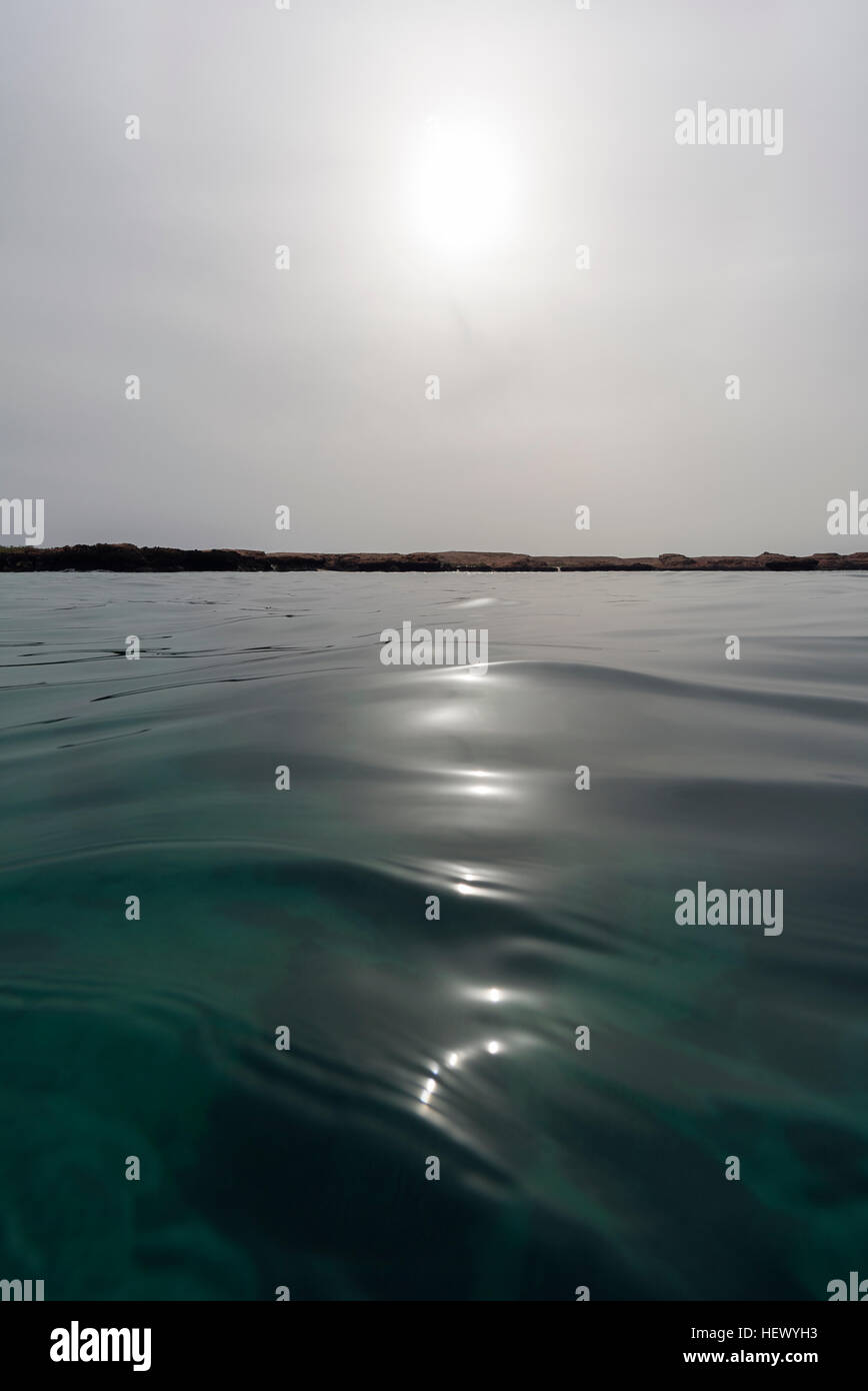 Eine schwache Sonne durchdringt einen grauen Himmel über einer ruhigen Meeresoberfläche in den Golf von Oman. Stockfoto