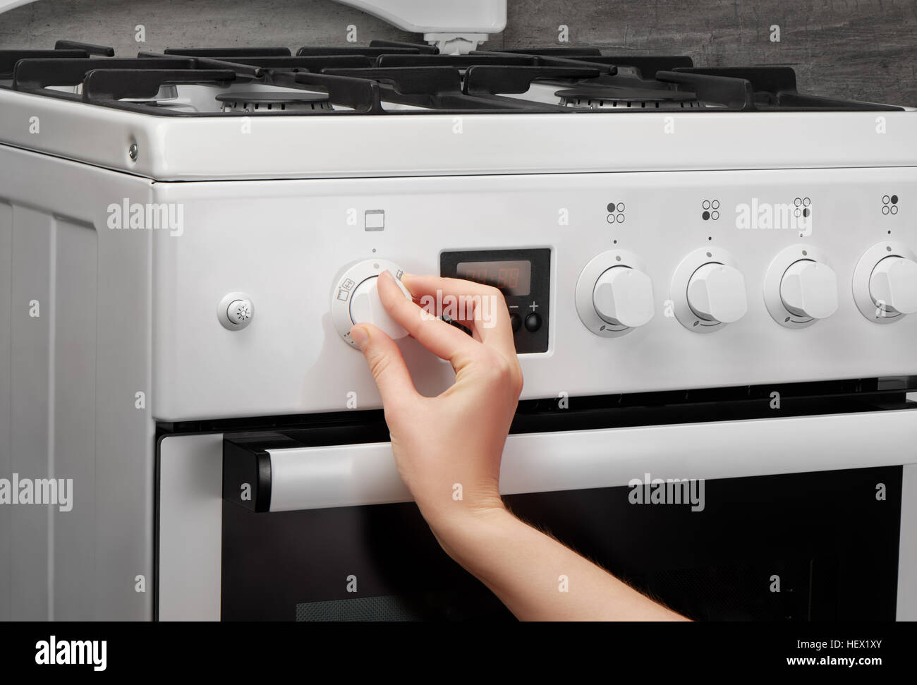 Weibliche Hand drehen auf weiße Küche Gasherd auf grauem Hintergrund Stockfoto
