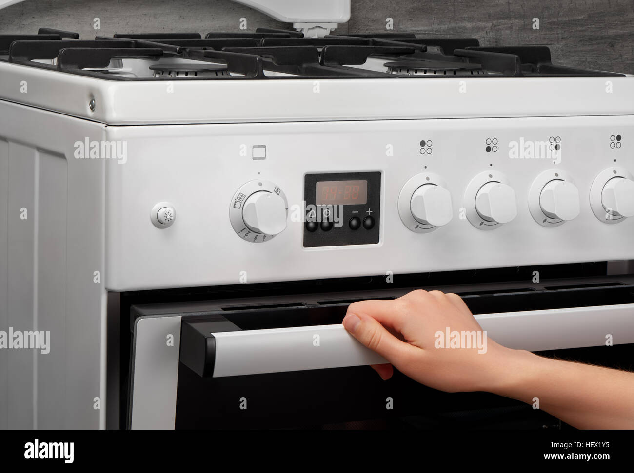 Weibliche Hand öffnen Ofen in weiße Küche Gasherd auf grauem Hintergrund Stockfoto