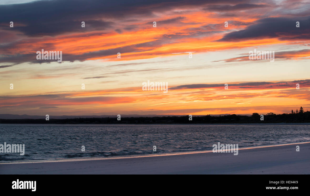 Die Sonne spiegelt sich auf den Wolken, wenn sie bei einem farbenprächtigen Sonnenuntergang in der Callala Bay in New South Wales, Australien, untergeht Stockfoto