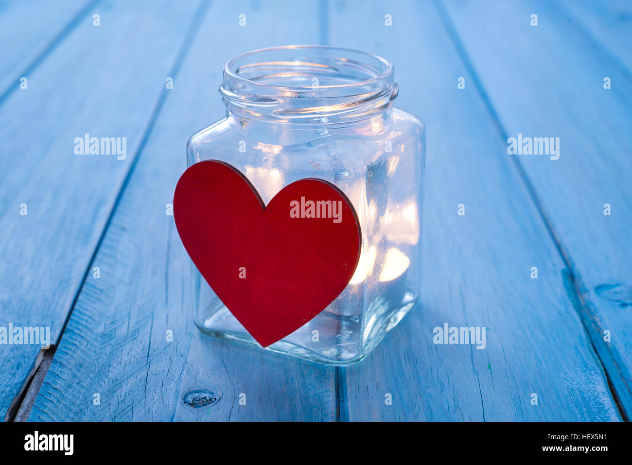 Glasdose mit einem roten Herzen und einer brennenden Kerze. Textfreiraum Stockfoto