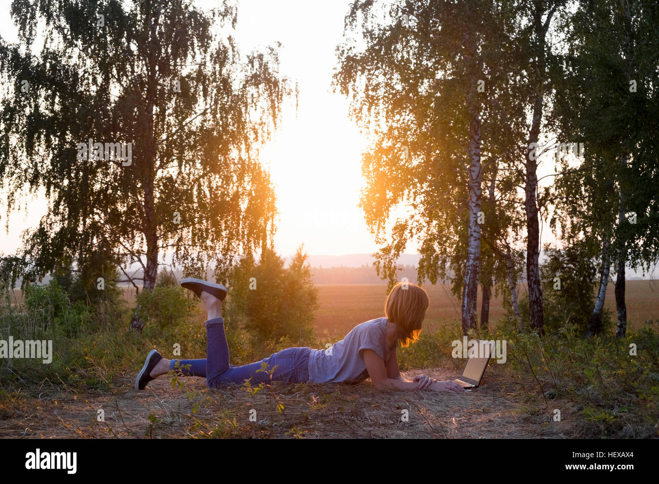Frau liegt am Rand des Feldes mit Laptop, Sonnenuntergang Stockfoto
