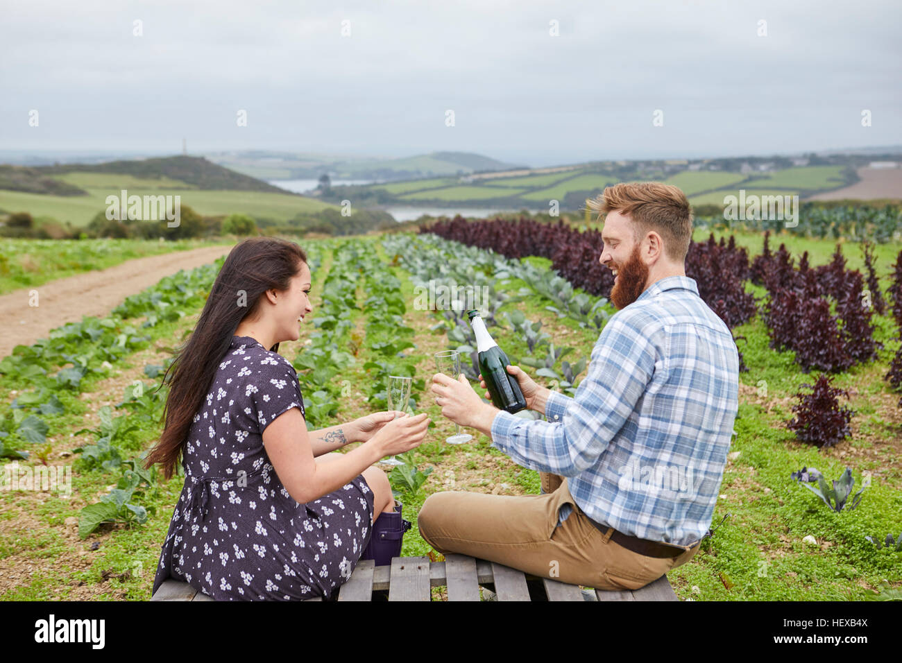 Paar in ländlicher Umgebung sitzen auf Paletten Champagner in Strömen Stockfoto