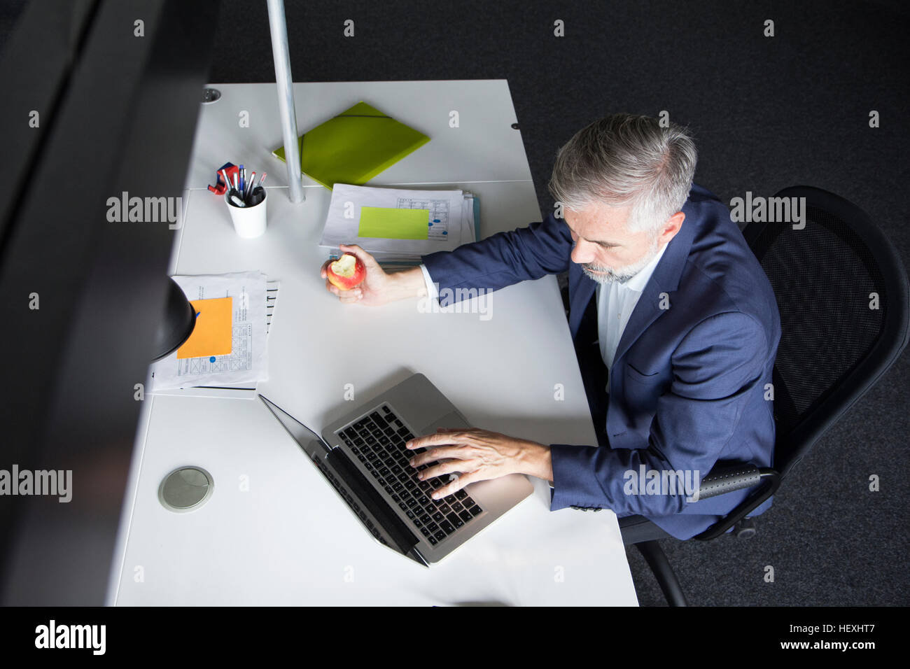 Geschäftsmann mit Laptop und Essen einen Apfel am Schreibtisch Stockfoto