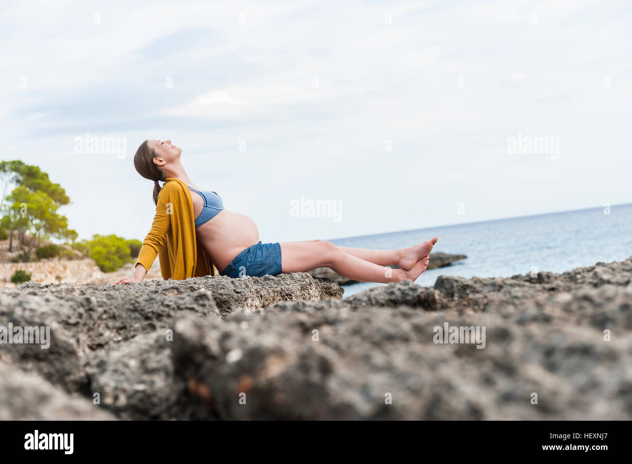 Schwangere Frau sitzen auf Felsen am Meer Stockfoto