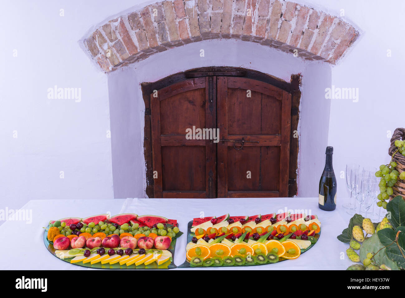 Zusammensetzung der Früchte und geschliffenem Glas Korbflasche beschichtet für Wein Wicker. Auf einem Tisch, beladen mit einem Restaurant, mit Trauben, Feigen, Kaktusfeigen und Blätter. A Stockfoto