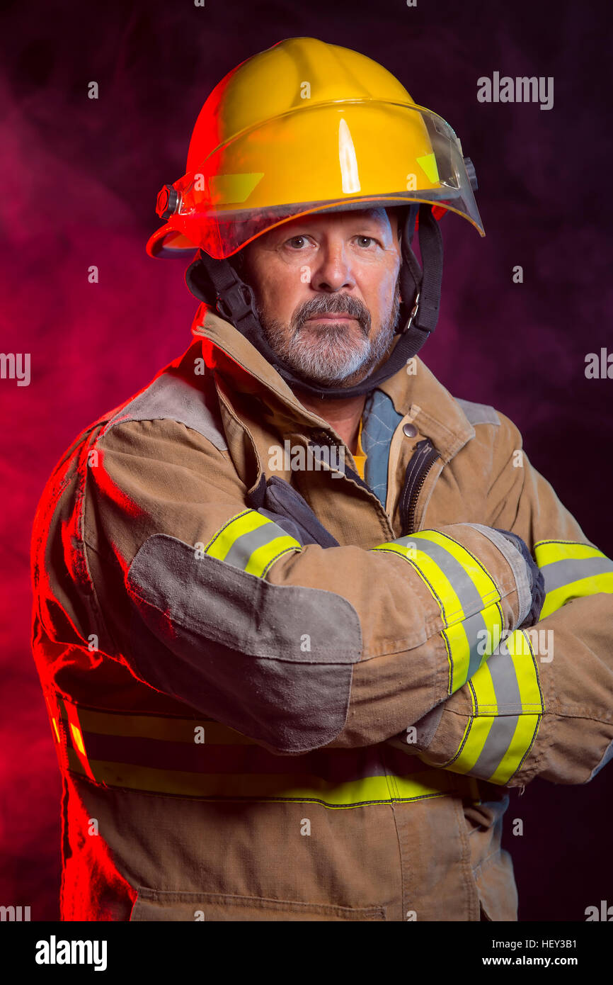 Porträt von einem Feuerwehrmann Feuerwehrmann weichen und Helm tragen. Hintergrund ist rot und blau, Rauch und Licht. Weichen sind schützen Stockfoto
