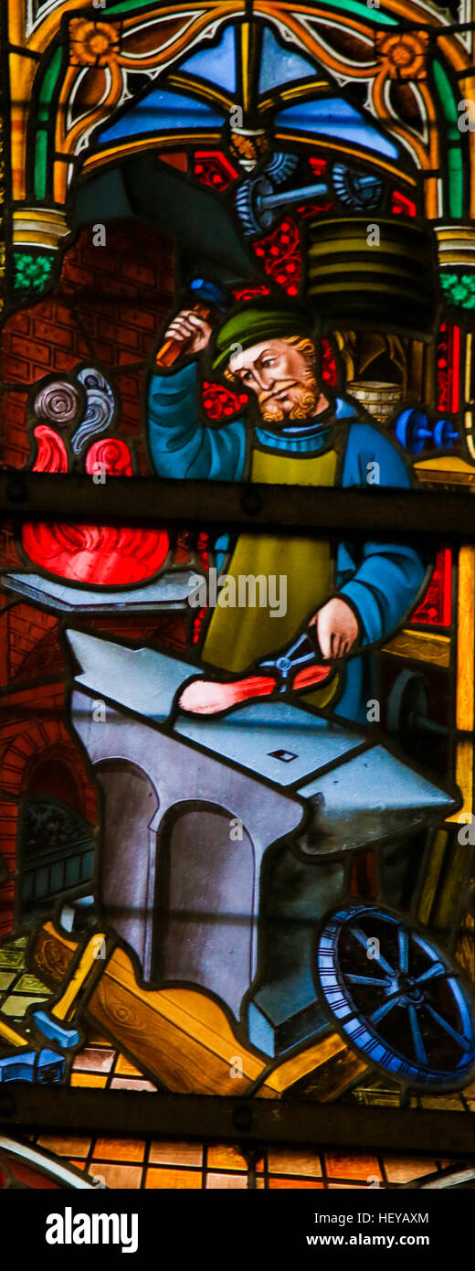 Glasmalerei-Fenster mit einem Schmied bei der Arbeit, in der Kathedrale St. Bavo in Gent, Flandern, Belgien. Stockfoto