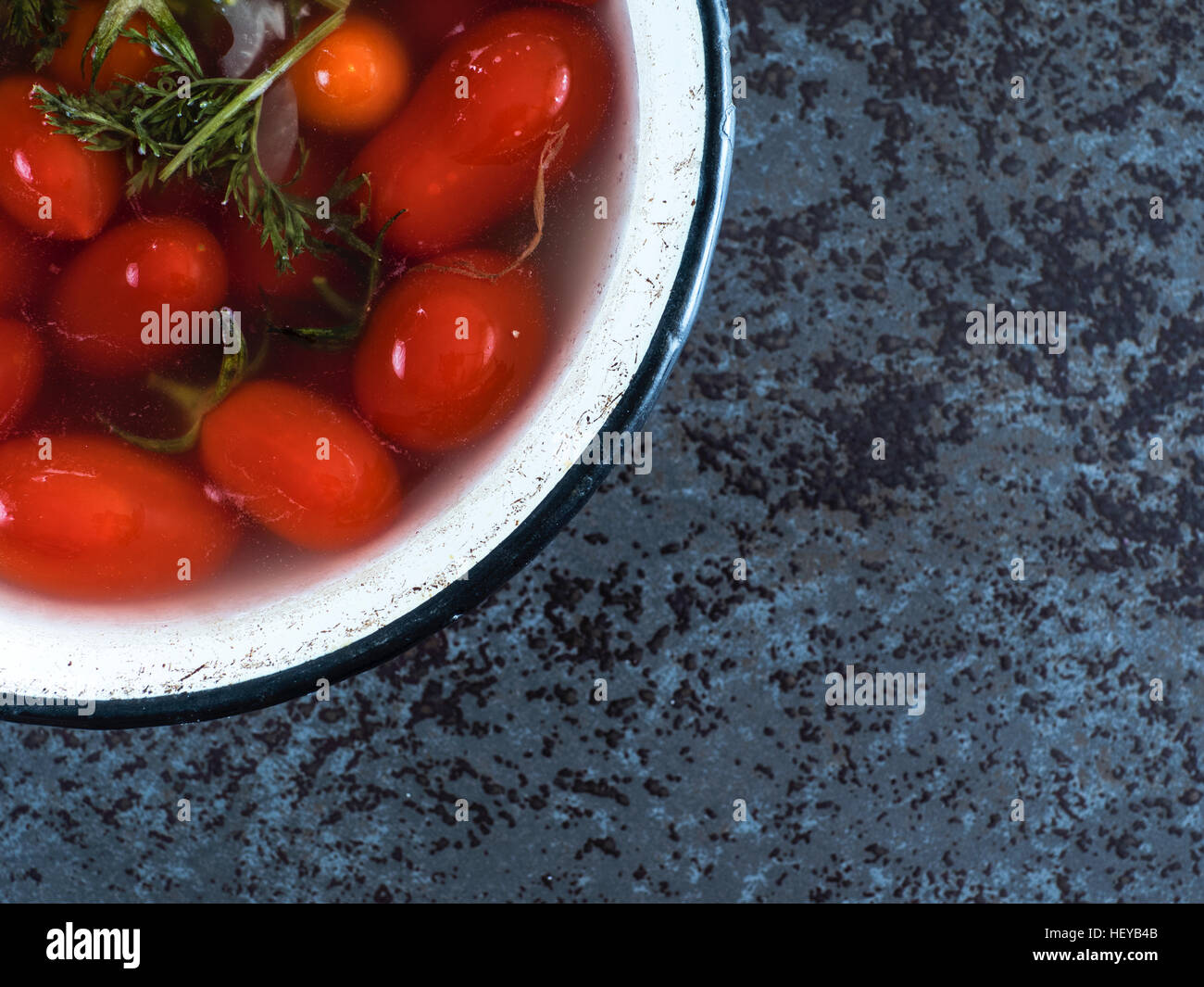 eingelegte Tomaten in emaillierte Metallschale auf dunklem Marmor Hintergrund Stockfoto