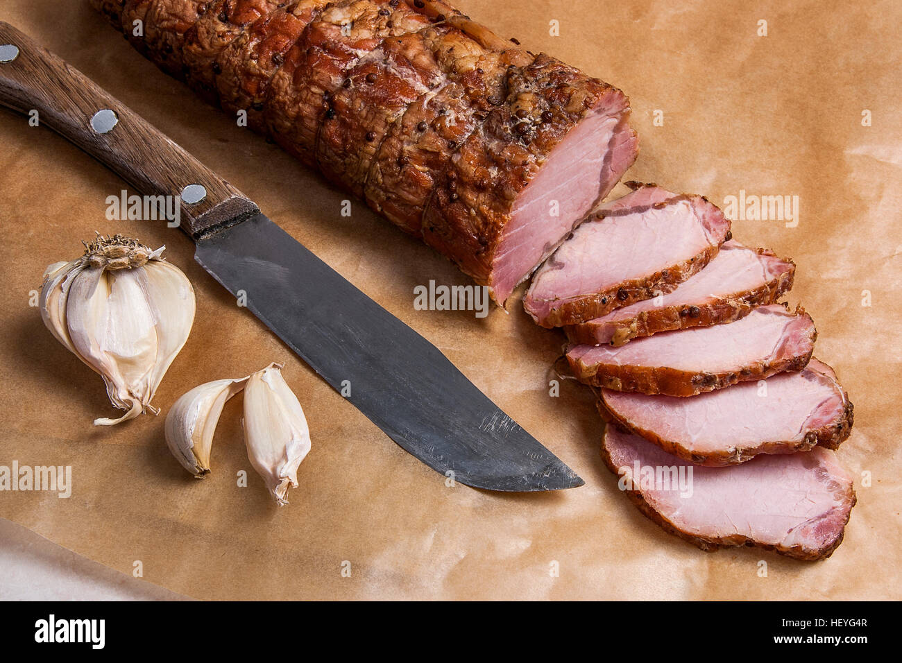 In Scheiben geschnitten mit Gewürzen und Kräutern Fleisch oder Schinken, altes Messer und Knoblauch geräuchert auf braunem Packpapier. Braune Tuch auf dem Rücken Hintergrund. Stockfoto